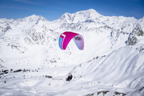 Parapentiste en rose survolant les montagnes enneigées de Belle Plagne près du Chalet des Cimes