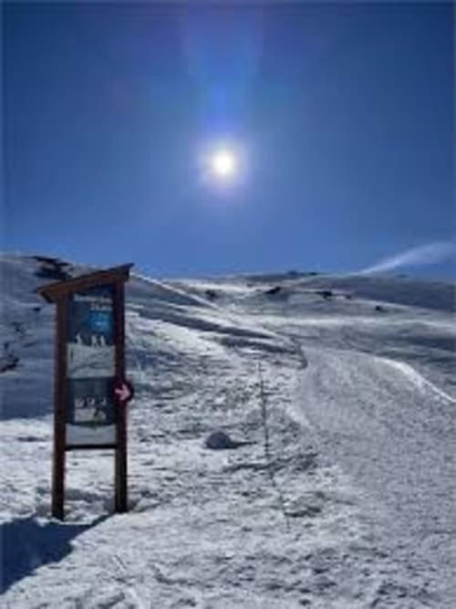Paysage alpin enneigé au Chalet des Cimes, Belle Plagne avec panneau en bois et soleil brillant