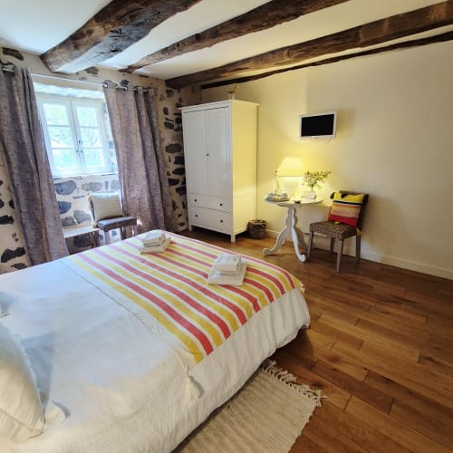 Chambre douillette au Mas De Rigoulac avec poutres apparentes, literie rayée colorée et vue sur le jardin à Argences-en-Aubrac