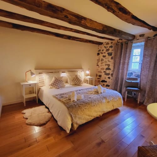 Chambre accueillante au Mas De Rigoulac avec poutres apparentes, lits jumeaux, mur en pierre et vue sur le jardin