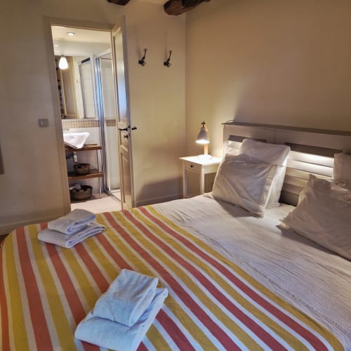 Chambre douillette au Mas De Rigoulac avec literie rayée colorée, salle de bain attenante et vue sur le jardin à Argences-en-Aubrac