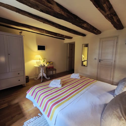 Chambre chaleureuse du Mas De Rigoulac avec lit rayé, poutres apparentes et vue sur le jardin