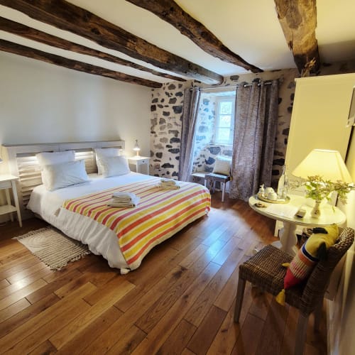 Chambre cosy au Mas De Rigoulac avec poutres apparentes, linge rayé et vue sur le jardin à Argences-en-Aubrac
