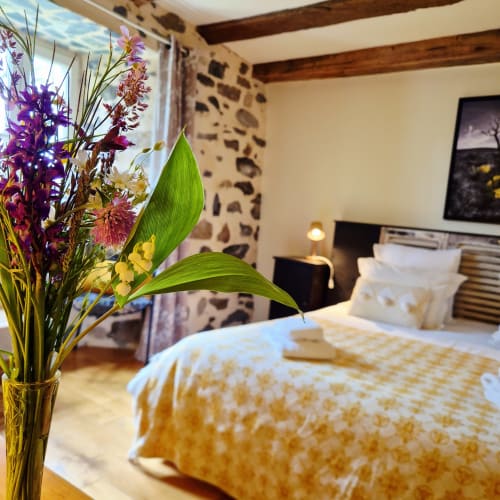 Chambre zen au Mas De Rigoulac avec fleurs violettes, poutres en bois et vue sur le jardin en Aubrac