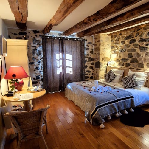Chambre rustique au Mas De Rigoulac avec poutres apparentes, murs en pierre et vue sur le jardin à Argences-en-Aubrac