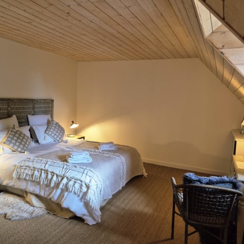 Chambre moderne à Argences-en-Aubrac avec plafond mansardé en bois, lit bien fait, éclairage fonctionnel et revêtement tissé au Mas