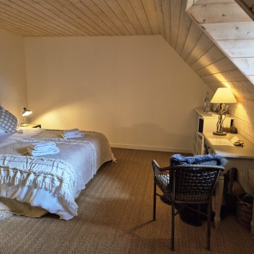Chambre douillette sous les combles au Mas De Rigoulac avec plafond en bois incliné, lit aux draps blancs, bureau et lampe