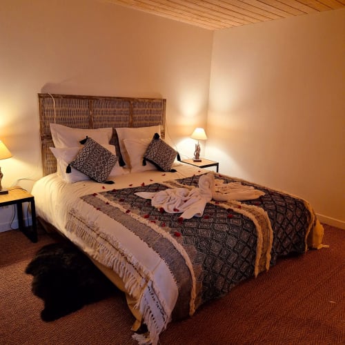 Chambre élégante au Mas De Rigoulac avec tête de lit tissée, pétales de rose romantiques, coussins à motifs et ambiance chaleureuse