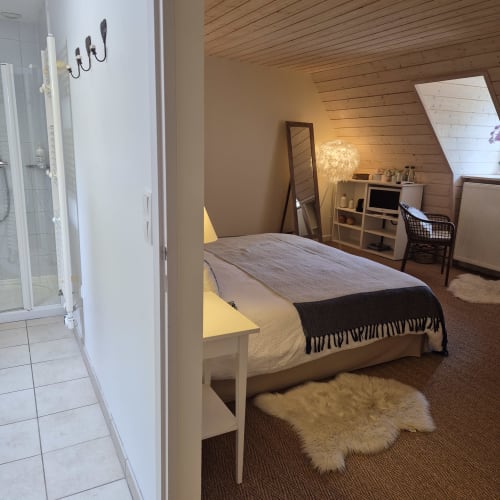 Chambre douillette mansardée au Mas De Rigoulac avec lit blanc, plafond en bois, bureau, miroir et salle de bain attenante