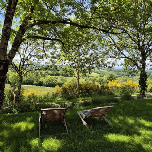 Deux chaises longues en bois sous les arbres surplombent les vallées verdoyantes du Mas De Rigoulac, Argences-en-Aubrac
