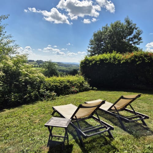 Deux chaises longues avec tables d'appoint sur une pelouse verdoyante ensoleillée avec vue sur la campagne ondulante du Mas De Rigoulac