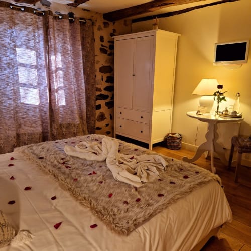 Chambre cosy du B&B Le Mas de Rigoulac avec pétales de roses, plaid moelleux, literie crème, TV et ambiance chaleureuse
