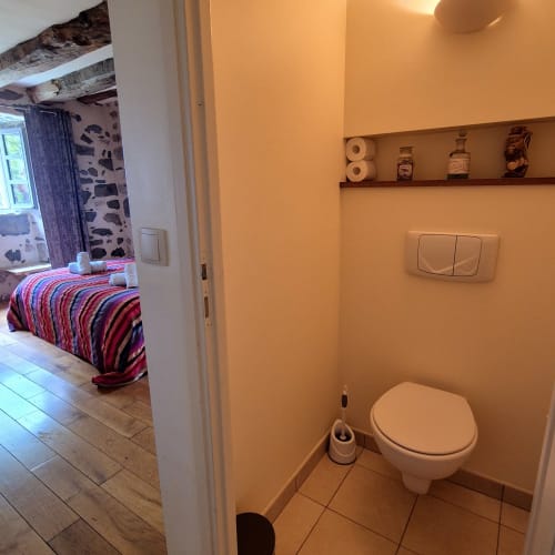 Salle de bains du gîte Le Mas De Rigoulac à Argences-en-Aubrac, aux murs pêche, avec toilettes et étagères décoratives
