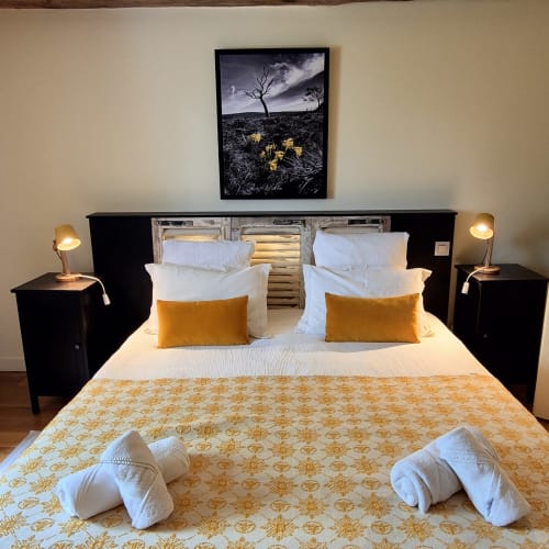 Chambre zen au Mas De Rigoulac avec lit queen-size, accents dorés, tête de lit noire et œuvres d'art offrant une vue sérène sur le jardin.