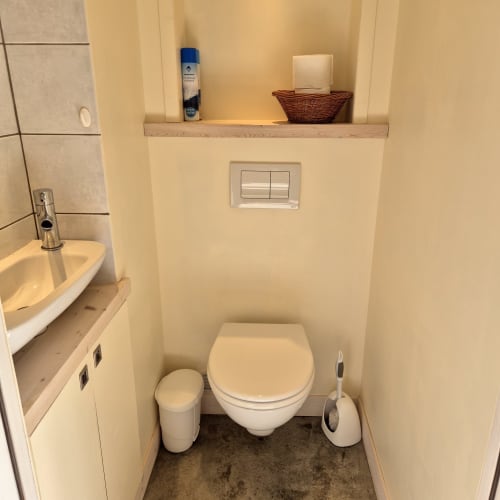 Salle de bains moderne du gîte Le Four au Mas De Rigoulac avec toilettes murales, lavabo et rangements en étagère