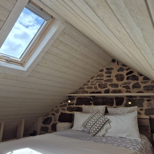 Chambre douillette sous les combles du Gîte Le Four : pierres apparentes, poutres bois, velux et vue sur le jardin à Argences-en-Aubrac
