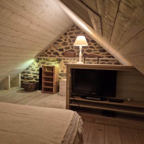 Chambre cosy sous les toits au gîte Le Mas De Rigoulac avec murs en pierre, poutres, TV, lampe et lit à Argences-en-Aubrac