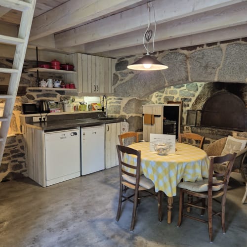 Cuisine rustique en pierre et salle à manger avec poutres apparentes, mobilier en bois et foyer traditionnel au Mas De Rigoulac