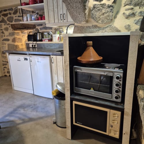 Cuisine du gîte Le Four avec tajine en terre cuite, four, lave-vaisselle et murs en pierre du Mas De Rigoulac