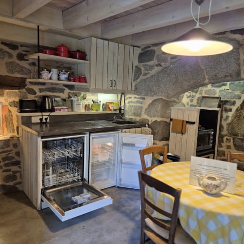 Cuisine rustique en pierre avec électroménagers modernes, salle à manger avec nappe à carreaux jaunes, Gîte Le Four au Mas De
