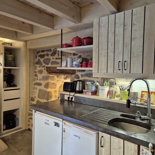 Petite cuisine moderne du Gîte Le Four au Mas De Rigoulac : murs en pierre, meubles bois, plan de travail sombre et