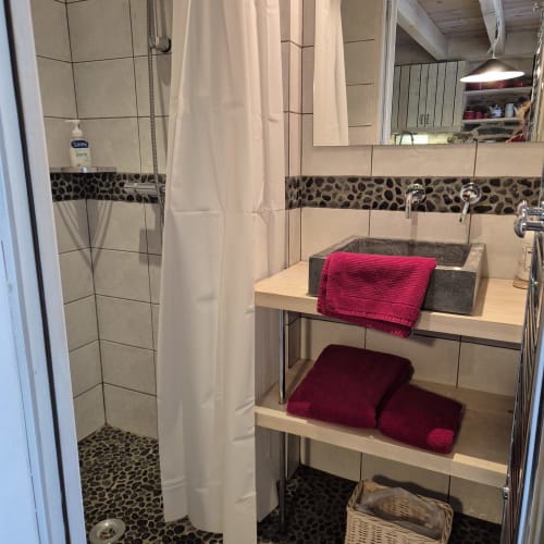 Salle de bains moderne du gîte Le Mas De Rigoulac avec carrelage galets, douche à l'italienne, vasque et serviettes bordeaux sur bois