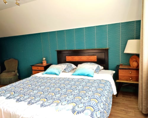 Chambre avec murs à motifs turquoise, lit à structure noire, tables de nuit orange et coussins bleus à la villa L'effet Mer Parenthese