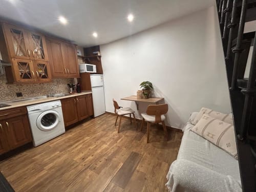 Acogedora cocina y sala de estar con muebles de madera, lavadora, mesa de comedor y cama en Casa de la Aguadora