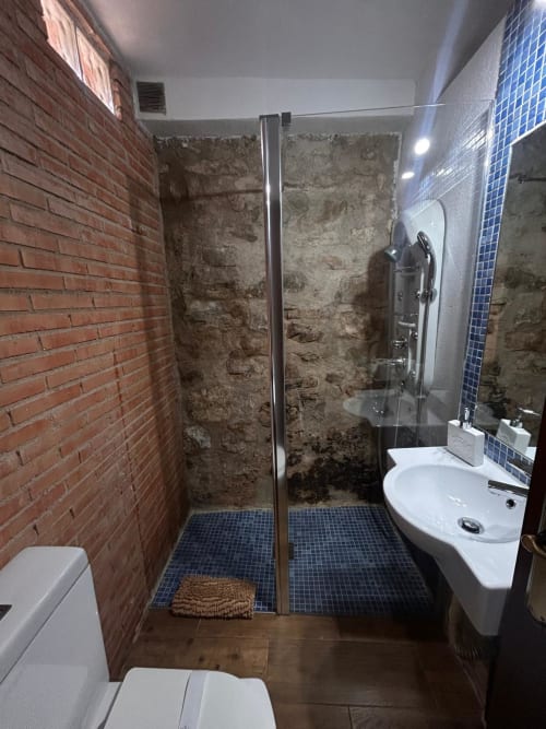 Baño moderno con ducha, lavamanos, azulejos de mosaico azul y pared de ladrillo visto en la casa rural Casa de la Aguadora, Iznatoraf