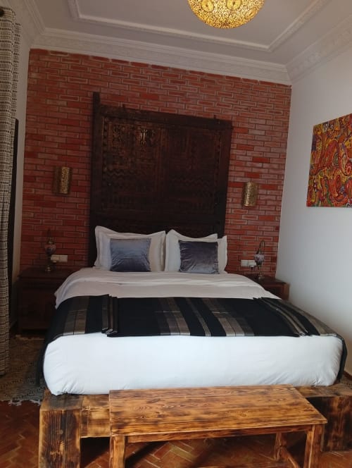 Chambre luxueuse du Riad Le Village Mogador à Essaouira avec lit en bois sombre, mur en brique rouge et literie blanche
