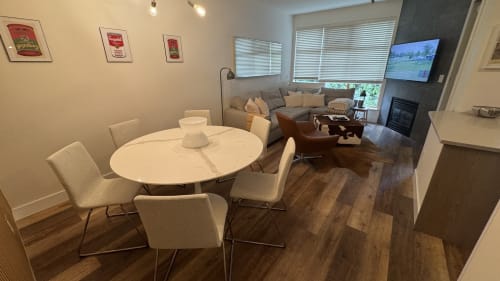 Modern apartment dining and living area in Whistler with round white table, cream chairs, gray sofa, fireplace, and mountain