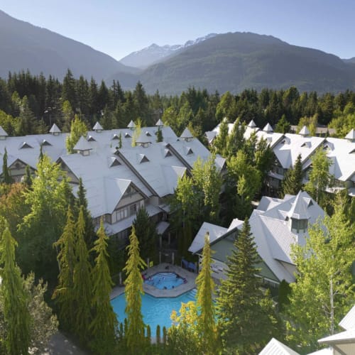 Whistler mountain resort with white-roofed chalets nestled among pine trees, featuring turquoise pool and snow-capped peaks