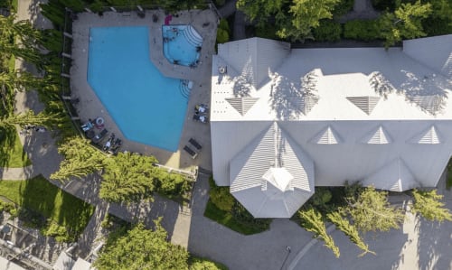 Aerial view of Whistler apartment complex with blue shared pool, hot tub, modern architecture, and surrounding green trees