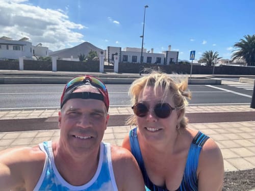 Two guests smiling at Villa Estrella Polar in Tahiche, with road and Mediterranean architecture in background