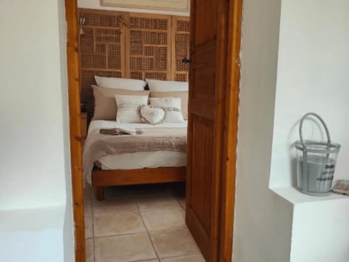 Schlafzimmer im Domaine Bellavigne Gîtes et Spa in Forcalquier mit Holzbett und gewebtem Kopfteil, Blick durch die Türöffnung