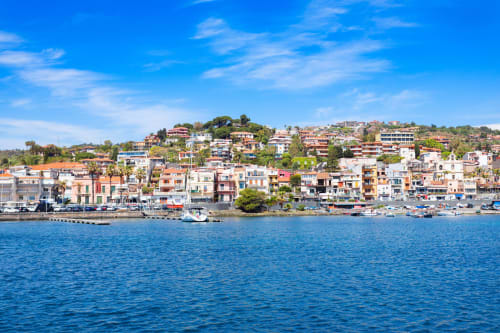 Case colorate sul waterfront di Aci Castello, Sicilia con vista sulle acque blu del Mediterraneo e barche, location di Fattoria dei