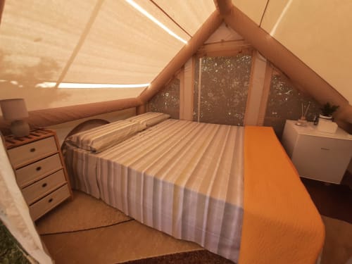 Camera da letto accogliente in tenda doppia presso Baia Dorica Camping Village con biancheria a righe, luce naturale, mobili in legno e arancione