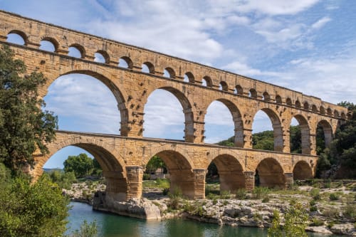 Historic stone aqueduct with arches spanning turquoise river near Aigues-Mortes, France
