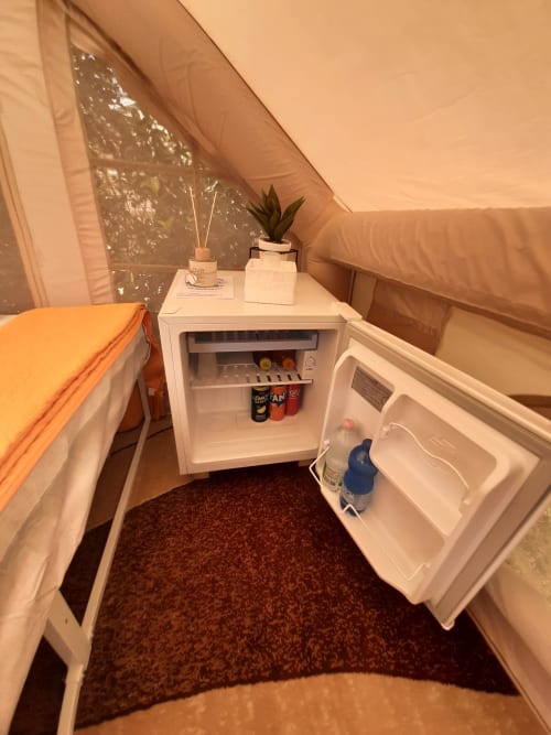Interno accogliente della tenda glamping a Baia Dorica con minibar, letto e piante in vaso