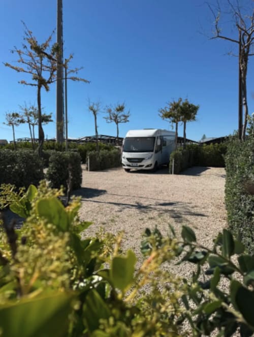 Camping-car blanc garé au Baia Dorica Camping Village à Vittoria, Italie, entouré de plantes méditerranéennes