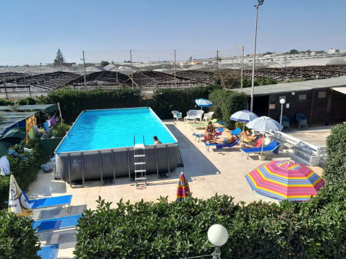 Zone de piscine du Camping Village Baia Dorica à Vittoria avec piscine rectangulaire bleue, parasols colorés et transats