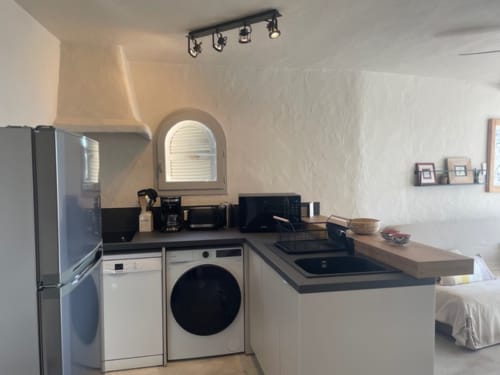 Kitchenette moderne à la Résidence Cala Di Sole avec électroménagers blancs, plan de travail noir et fenêtre cintrée à Lecci