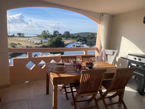 Terrasse d'appartement avec vue mer, table et chaises en bois, kitchenette visible, surplombant la marina de Lecci