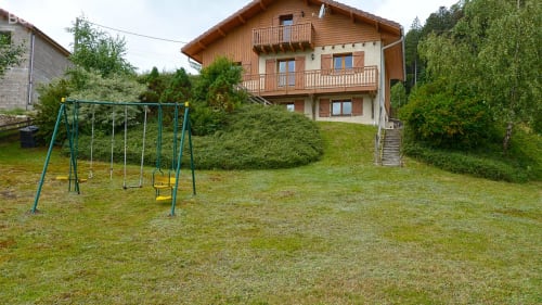 Chalet le Grizzli's backyard with children's swing set, green lawn, and wooden alpine-style cottage in Le Tholy, Vosges.