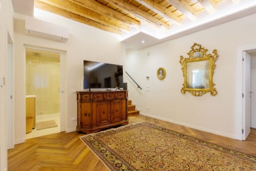 Elegant Venetian villa living room with herringbone wood floors, ornate gold mirror, wooden furniture, and modern flat-screen