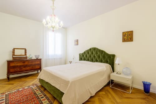 Elegant green headboard bedroom in Venice villa with wooden furniture, chandelier, and parquet flooring