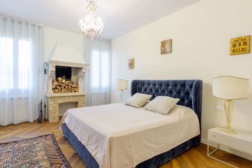 Elegant bedroom in Venice villa with fireplace, blue upholstered bed, chandelier, and classic decor