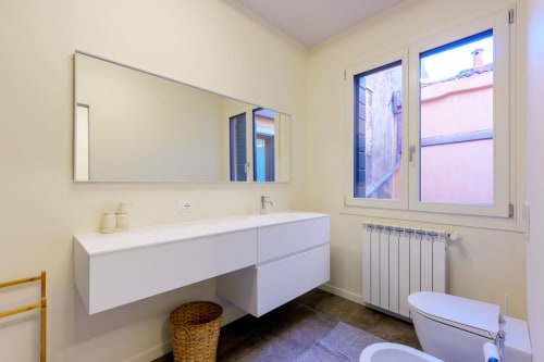 Modern bathroom in Bealux villa, Venice with white vanity, mirror, heated radiator, and window with landmark view
