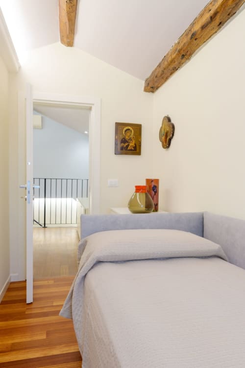 Modern Venetian villa bedroom with exposed wooden beams, religious artwork, and wooden floors