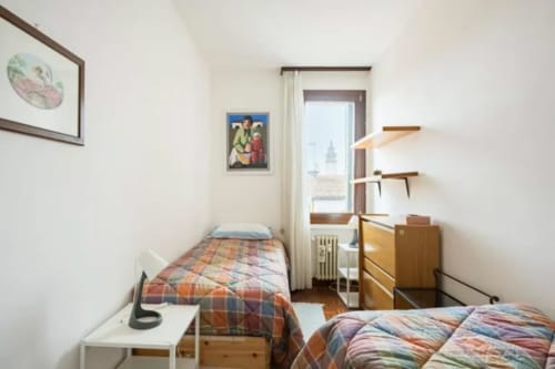 Cozy shared bedroom in Bealux Venice apartment with twin beds, wooden furniture, and canal view overlooking landmark